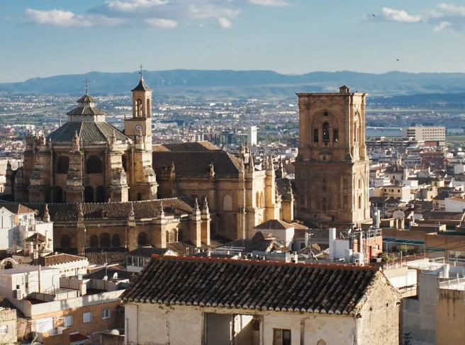 Vista a&eacute;rea de una catedral antigua rodeada de edificios y monta&ntilde;as al fondo.