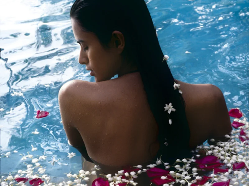 Mujer de espaldas en el agua con p&eacute;talos de flores flotando a su alrededor.