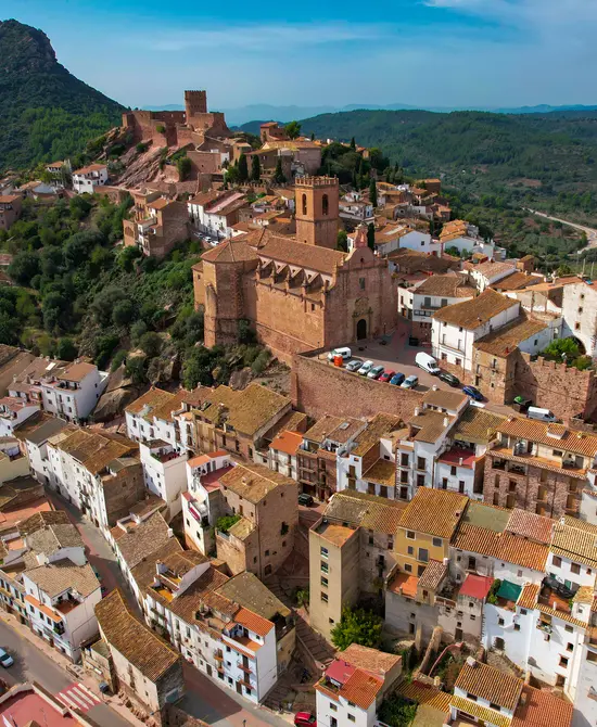 Vista aérea de un pueblo con iglesia y castillo en una colina.