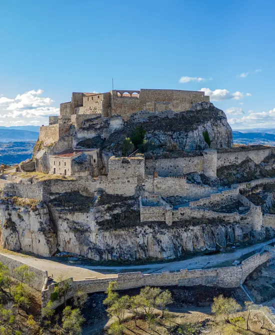 Castillo sobre colina rocosa con vista panorámica y cielo azul brillante.