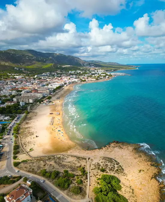 Vista aérea de una playa con aguas turquesas y una ciudad costera.
