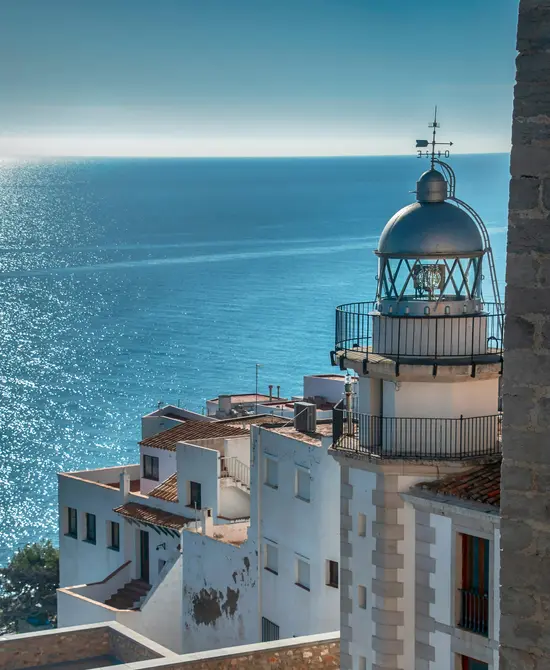 Faro junto a edificios blancos frente al mar azul bajo el cielo despejado.