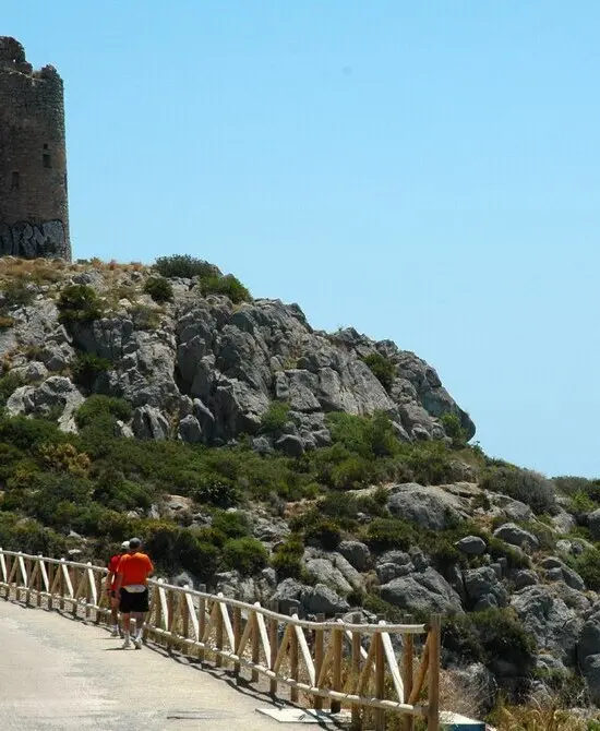 Persona caminando cerca de una colina rocosa con una torre antigua.