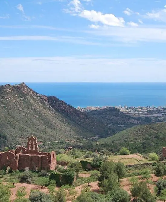 Ruinas en un valle montañoso junto al mar y una ciudad al fondo.