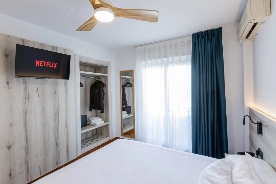 Habitación moderna con TV, armario abierto y cortinas azules.