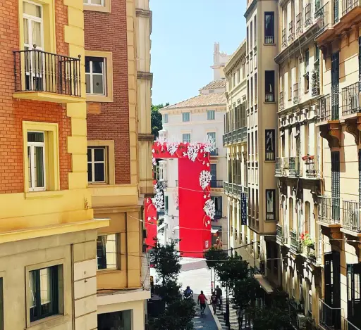 Calle estrecha entre edificios altos, un mural rojo al fondo con figuras blancas.
