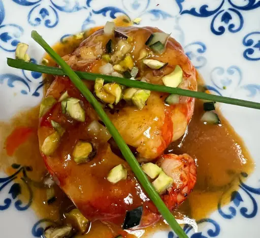 Langosta en salsa con trozos de pistacho y ceboll&iacute;n sobre plato decorado azul.