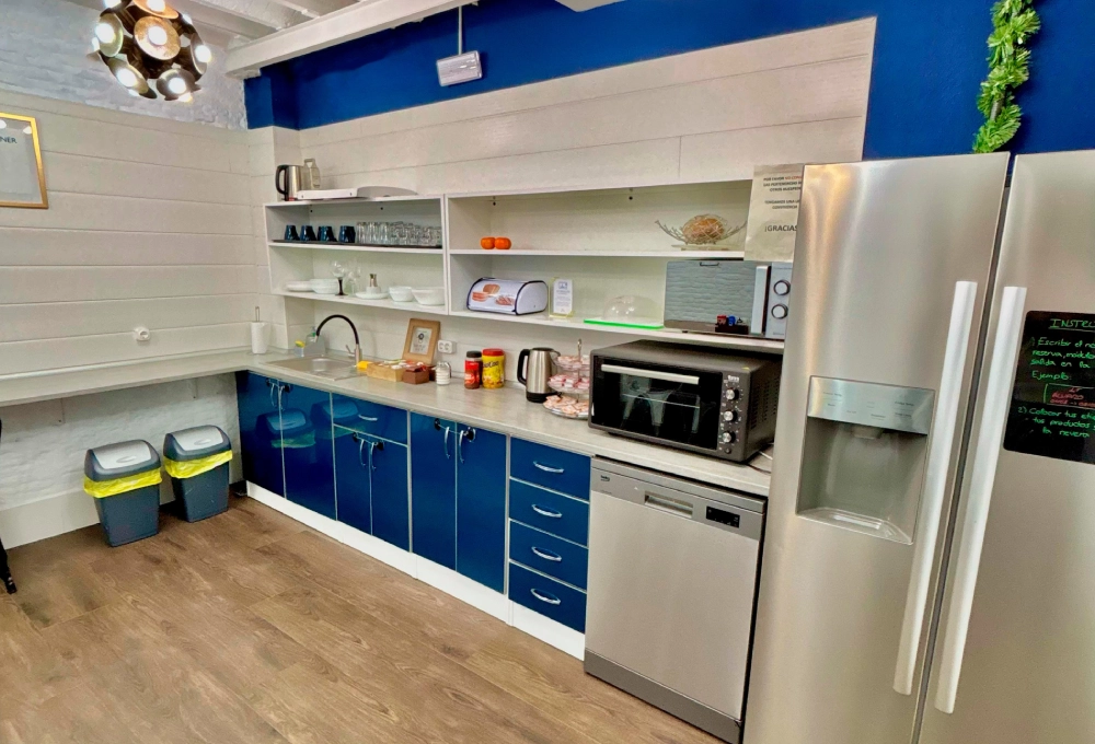 Cocina moderna con gabinetes azules, electrodom&eacute;sticos de acero y estantes con vajilla.