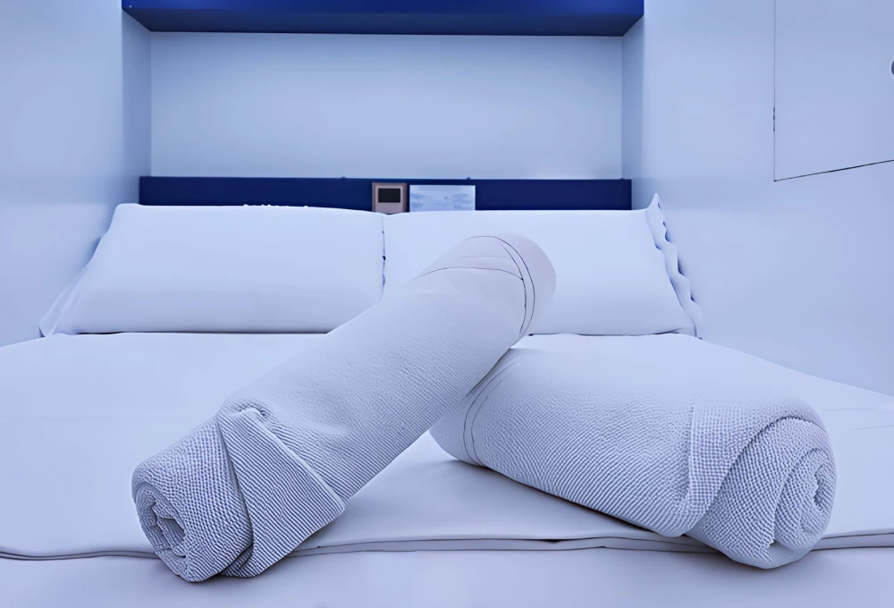 Cama moderna con s&aacute;banas blancas y almohadas cil&iacute;ndricas enrolladas en el centro.