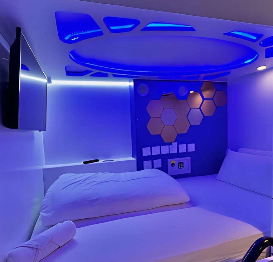 C&aacute;psula futurista iluminada en azul con cama, pantalla y paneles hexagonales.