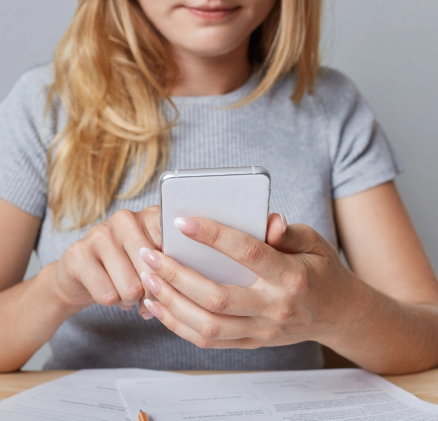 Mujer usando un tel&eacute;fono m&oacute;vil, con papeles sobre la mesa.