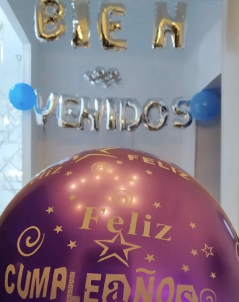 Globo morado de "Feliz cumplea&ntilde;os" y globos dorados que dicen "Bienvenidos" con detalles azules.