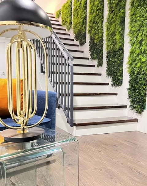 Escaleras con barandilla negra y paredes verdes, l&aacute;mpara dorada cerca de un sof&aacute; azul.