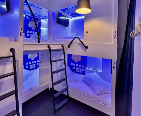 Literas modernas con iluminaci&oacute;n azul y escaleras en un hostal, ambientado con cortinas.