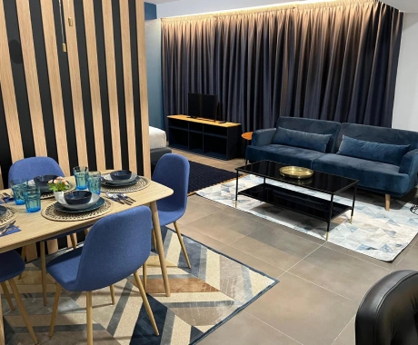 Sala moderna con sof&aacute; azul, mesa de comedor y cortinas oscuras, decorada en tonos azules y beige.