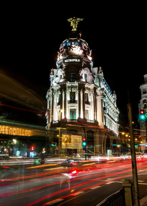 Edificio Metr&oacute;polis iluminado de noche en una intersecci&oacute;n con luces de tr&aacute;fico en movimiento.
