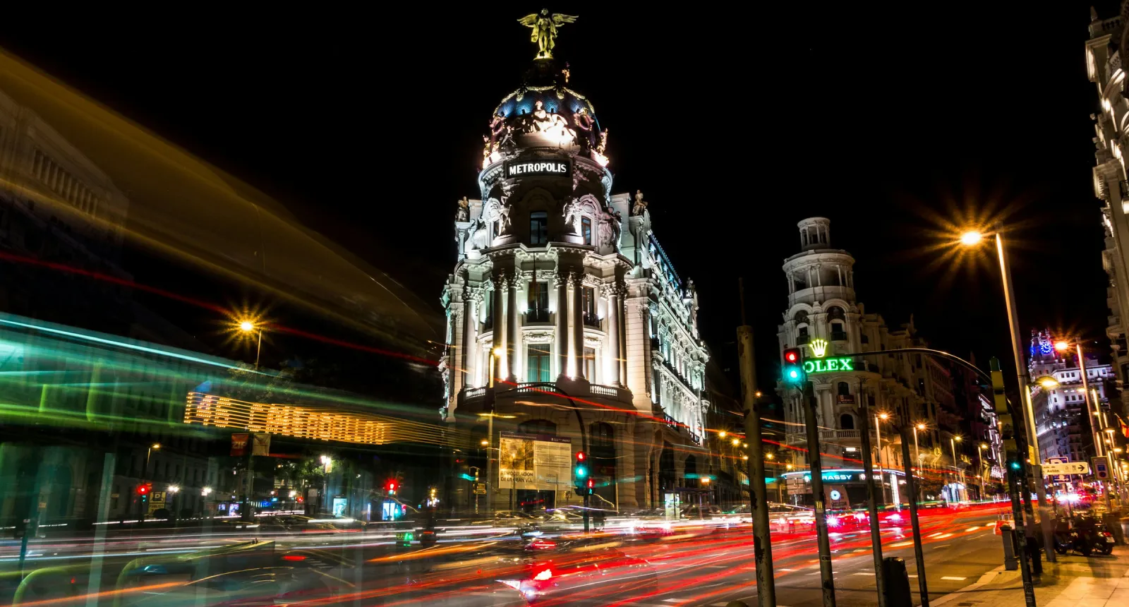 Larga exposici&oacute;n nocturna de una avenida en una ciudad con tr&aacute;fico y edificios iluminados.