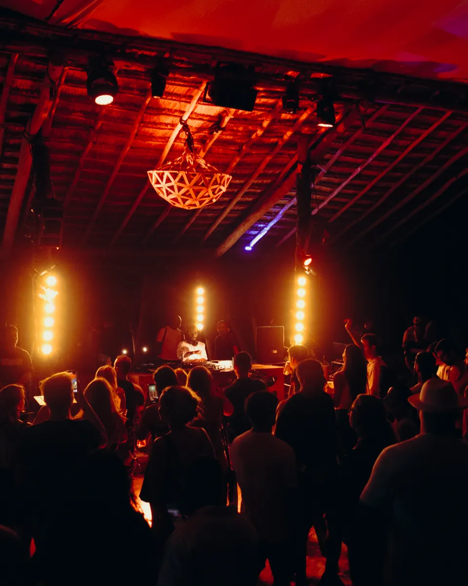 Personas disfrutando de un concierto bajo luces c&aacute;lidas en un escenario interior.
