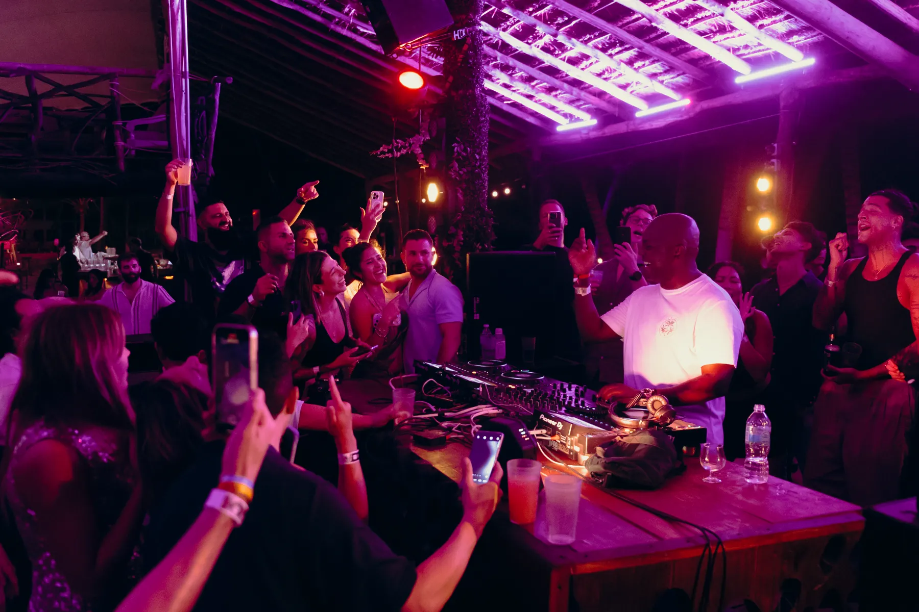 DJ animando a una multitud bajo luces púrpuras en una fiesta nocturna.