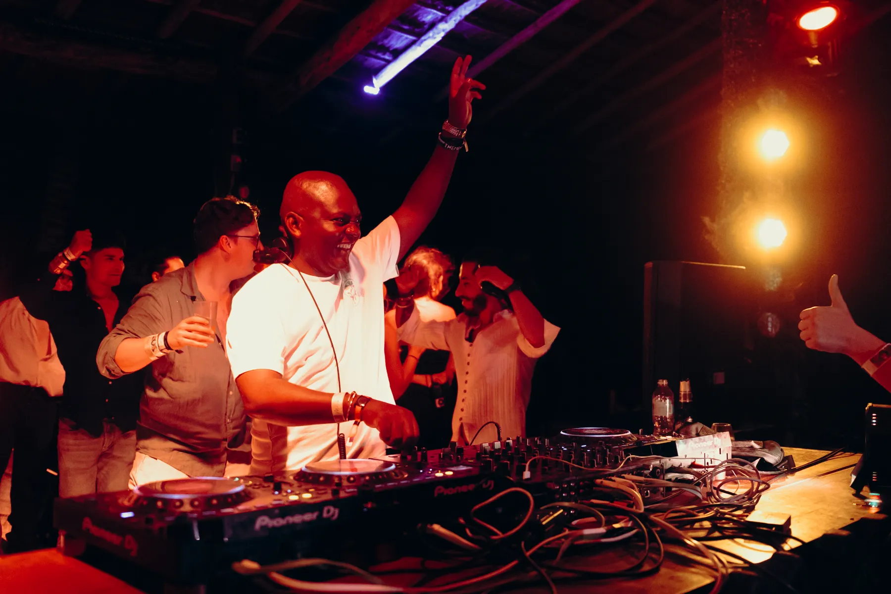 DJ sonriendo mientras toca en una fiesta nocturna, rodeado de personas bailando.