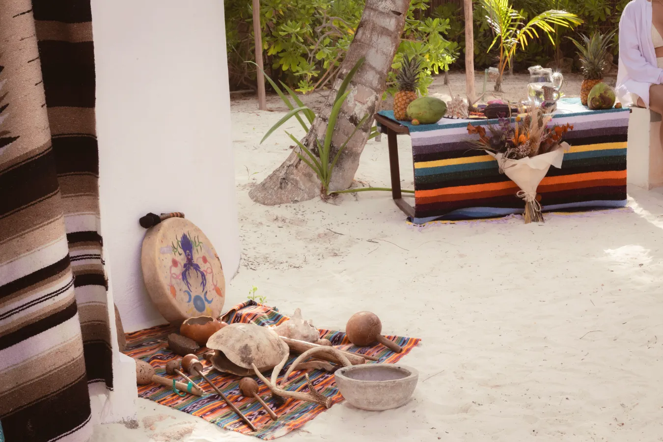 Objetos sobre mantas en una playa con decoraci&oacute;n colorida y vegetaci&oacute;n.