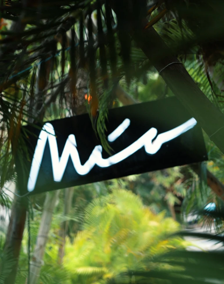 Cartel de ne&oacute;n con la palabra "M&iacute;o" rodeado de vegetaci&oacute;n exuberante.