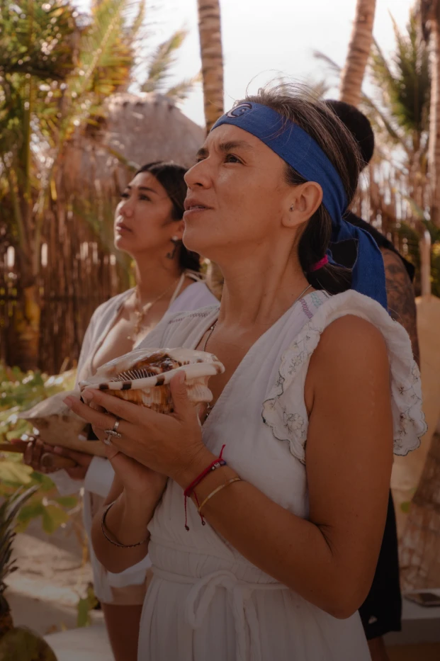 Mujeres participando en un ritual al aire libre, sosteniendo caracoles en las manos.