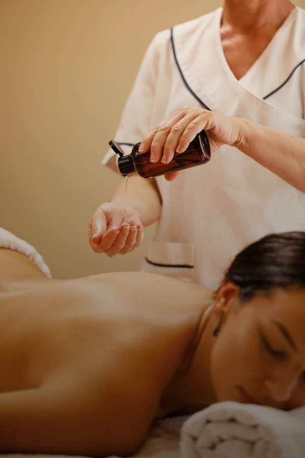 Terapeuta aplicando aceite en la mano para un masaje relajante en una mujer.