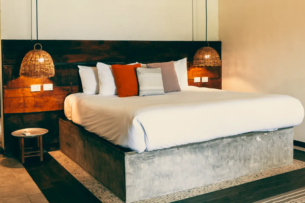 Cama con almohadas de colores y dos l&aacute;mparas colgantes en una habitaci&oacute;n.