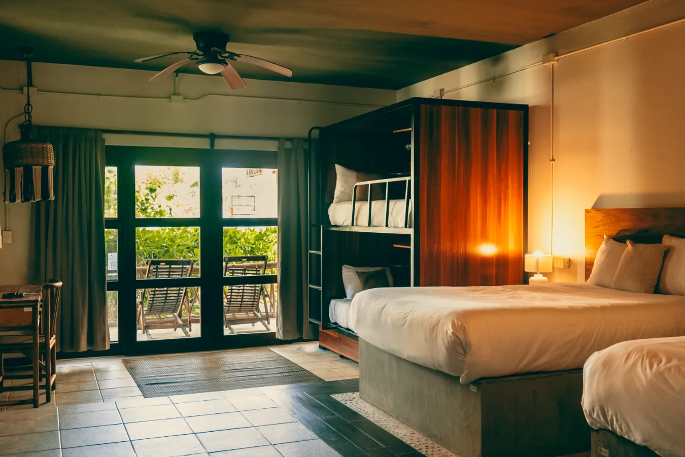 Habitaci&oacute;n amplia con camas, balc&oacute;n y luz c&aacute;lida al atardecer.