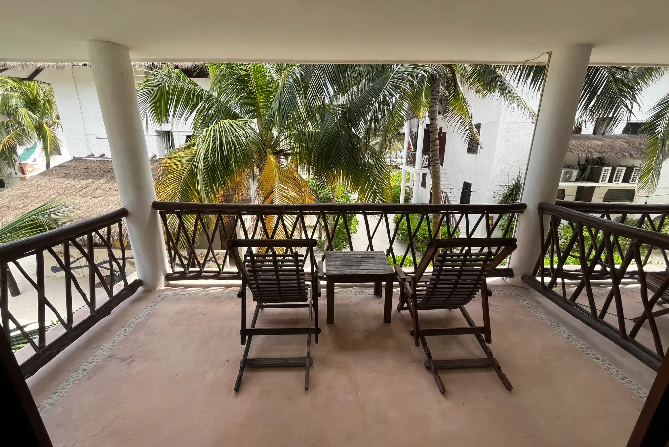 Balcón con sillas y mesa, vista de palmeras y edificios blancos.