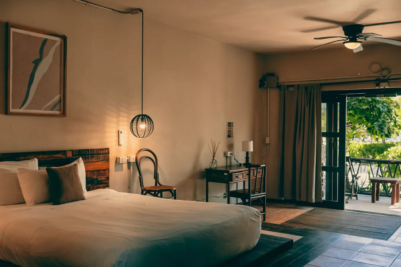 Habitación rústica con cama, escritorio y vista al jardín.