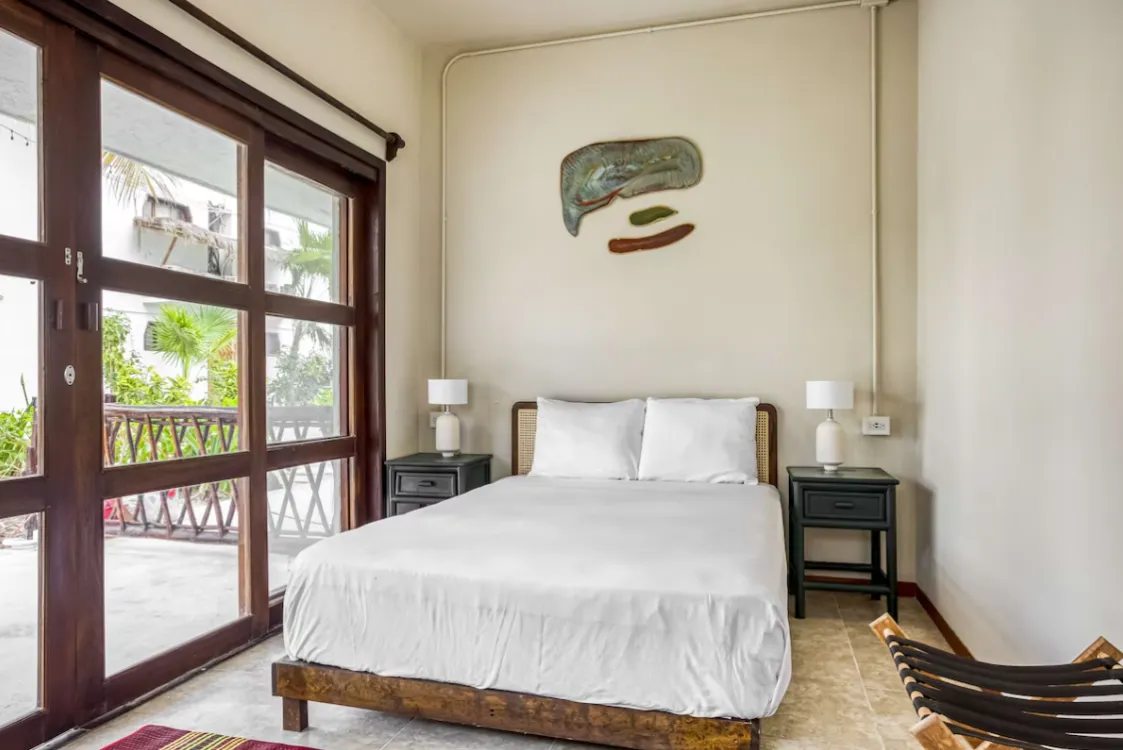 Habitación minimalista con cama, lámparas y puerta de vidrio al jardín.