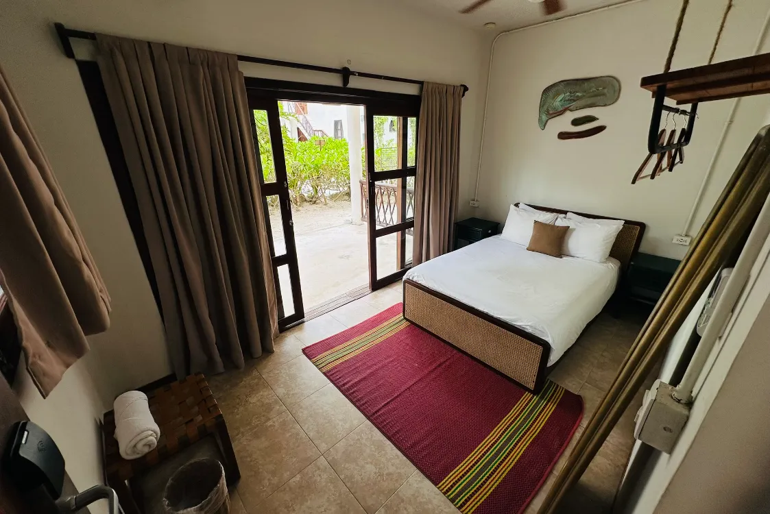 Habitación con cama, alfombra y puertas abiertas hacia el jardín.