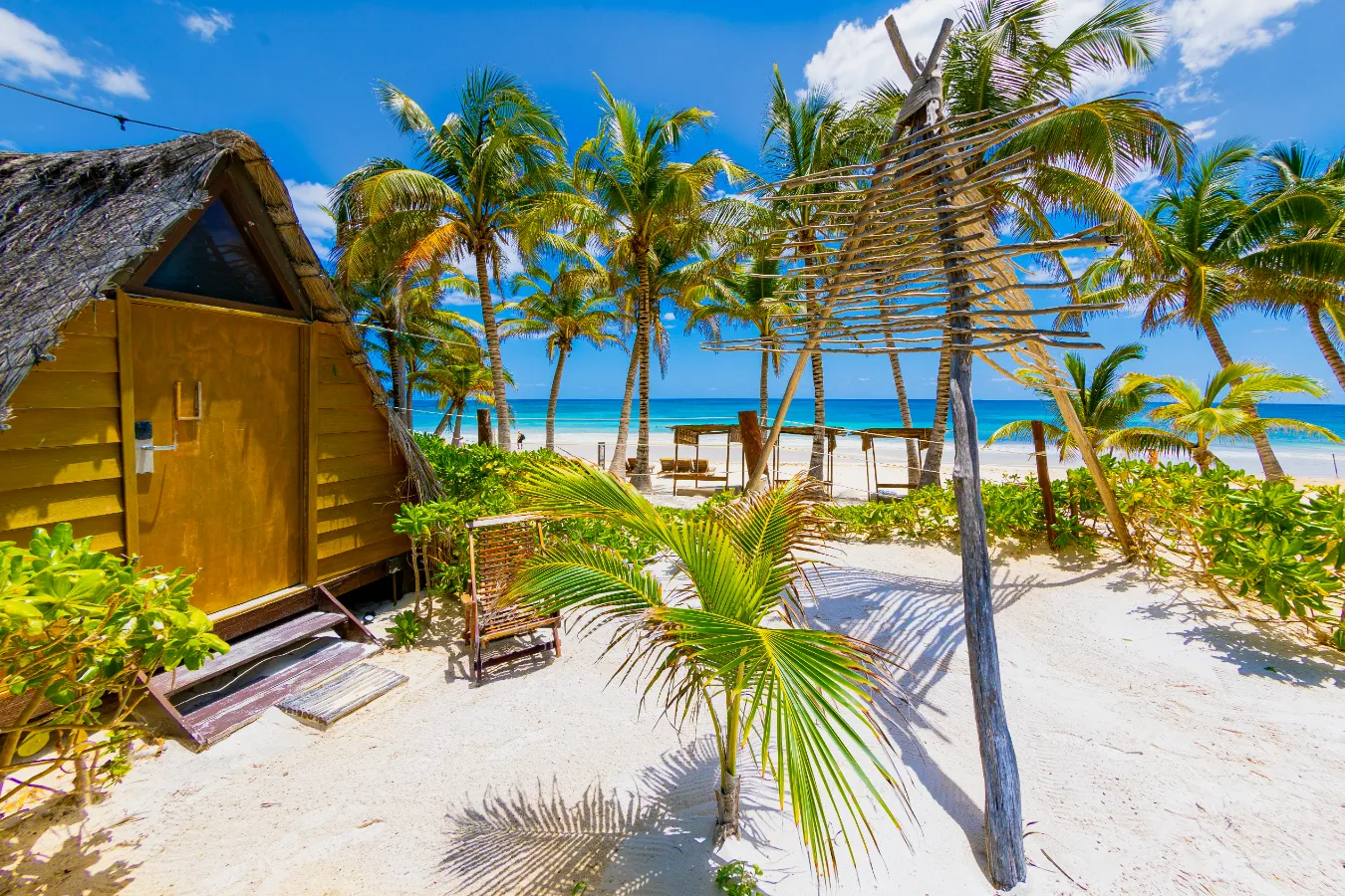 Cabaña y palmeras en una playa de arena blanca frente al mar turquesa.