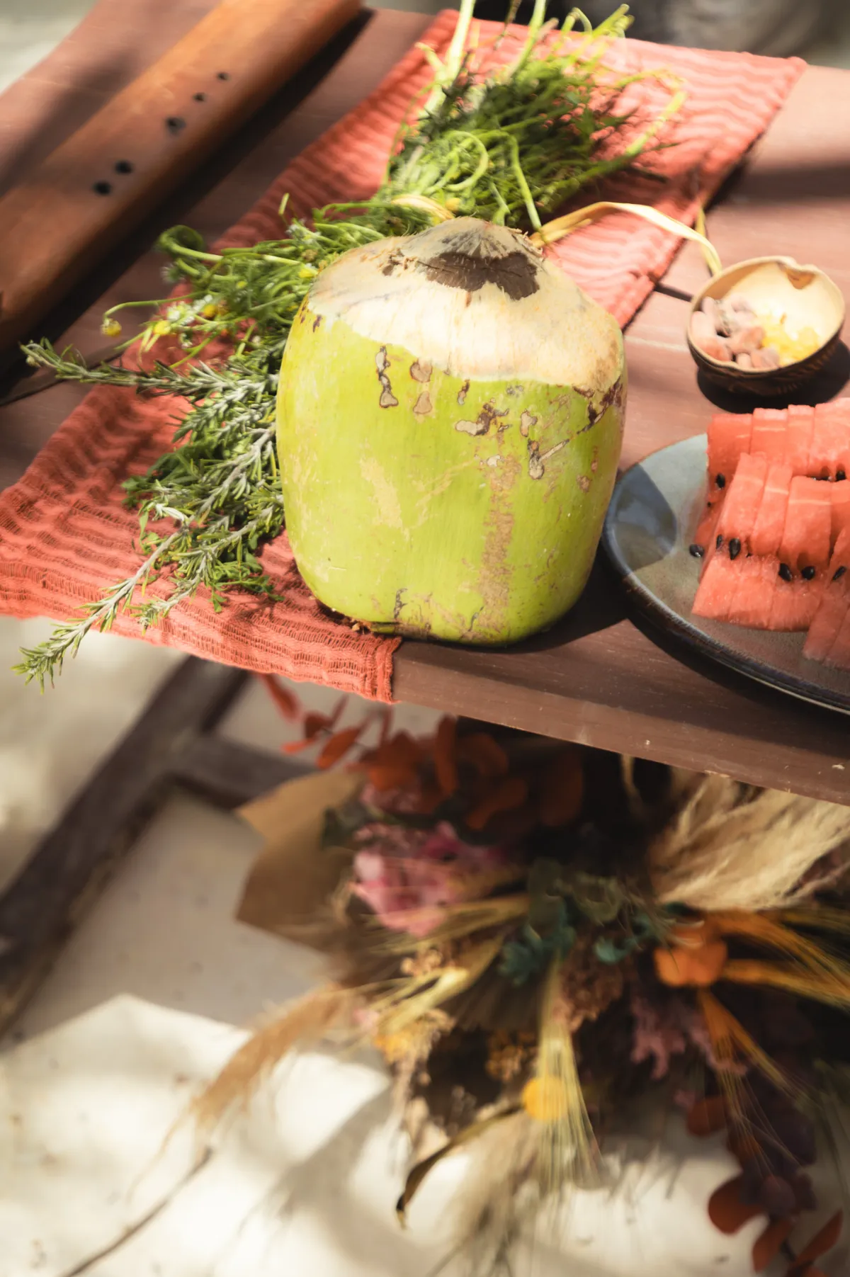 Coco, rodajas de sandía y hierbas en una mesa decorada rústicamente.