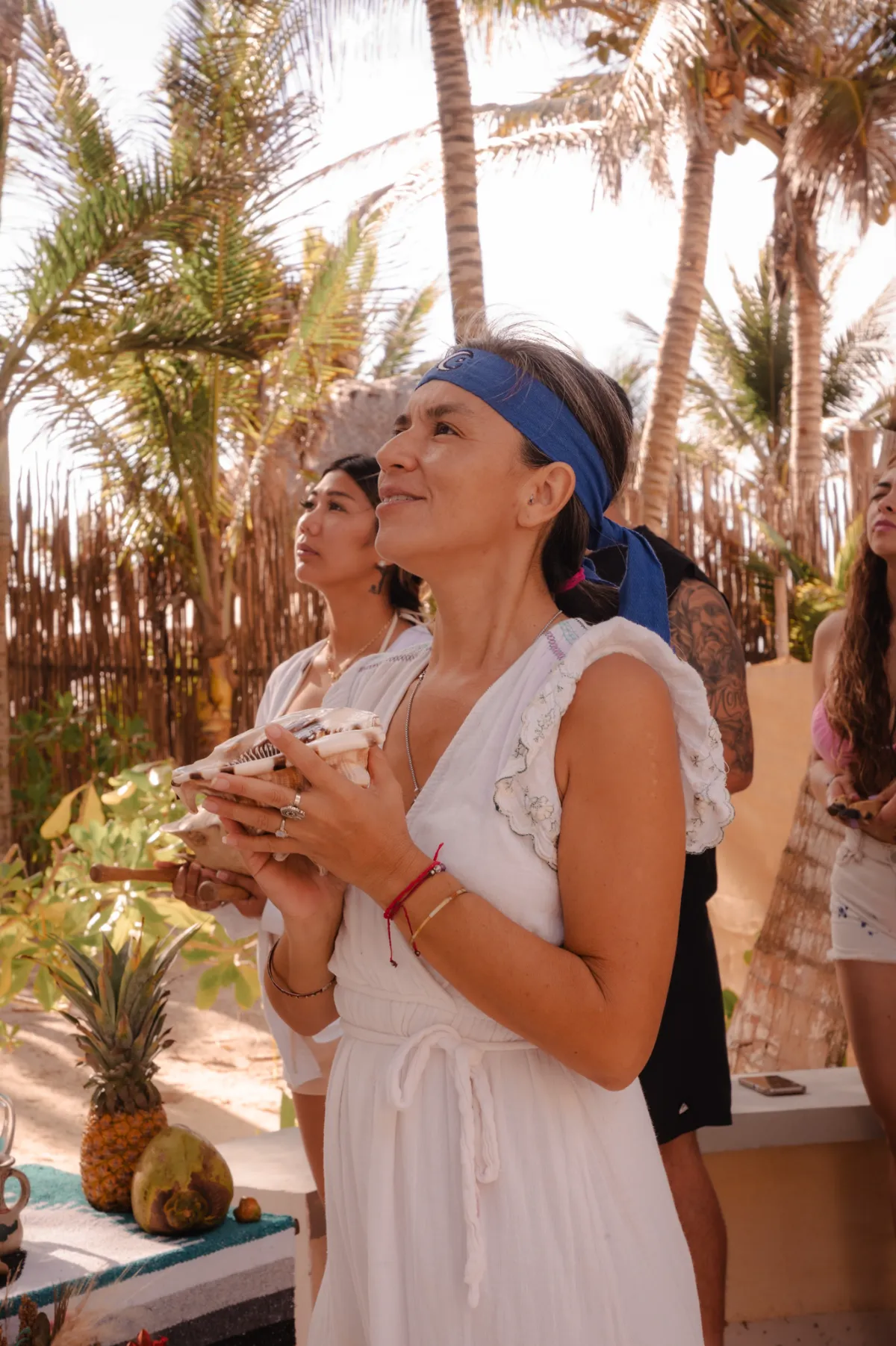 Personas en ceremonia espiritual al aire libre, rodeadas de palmeras.