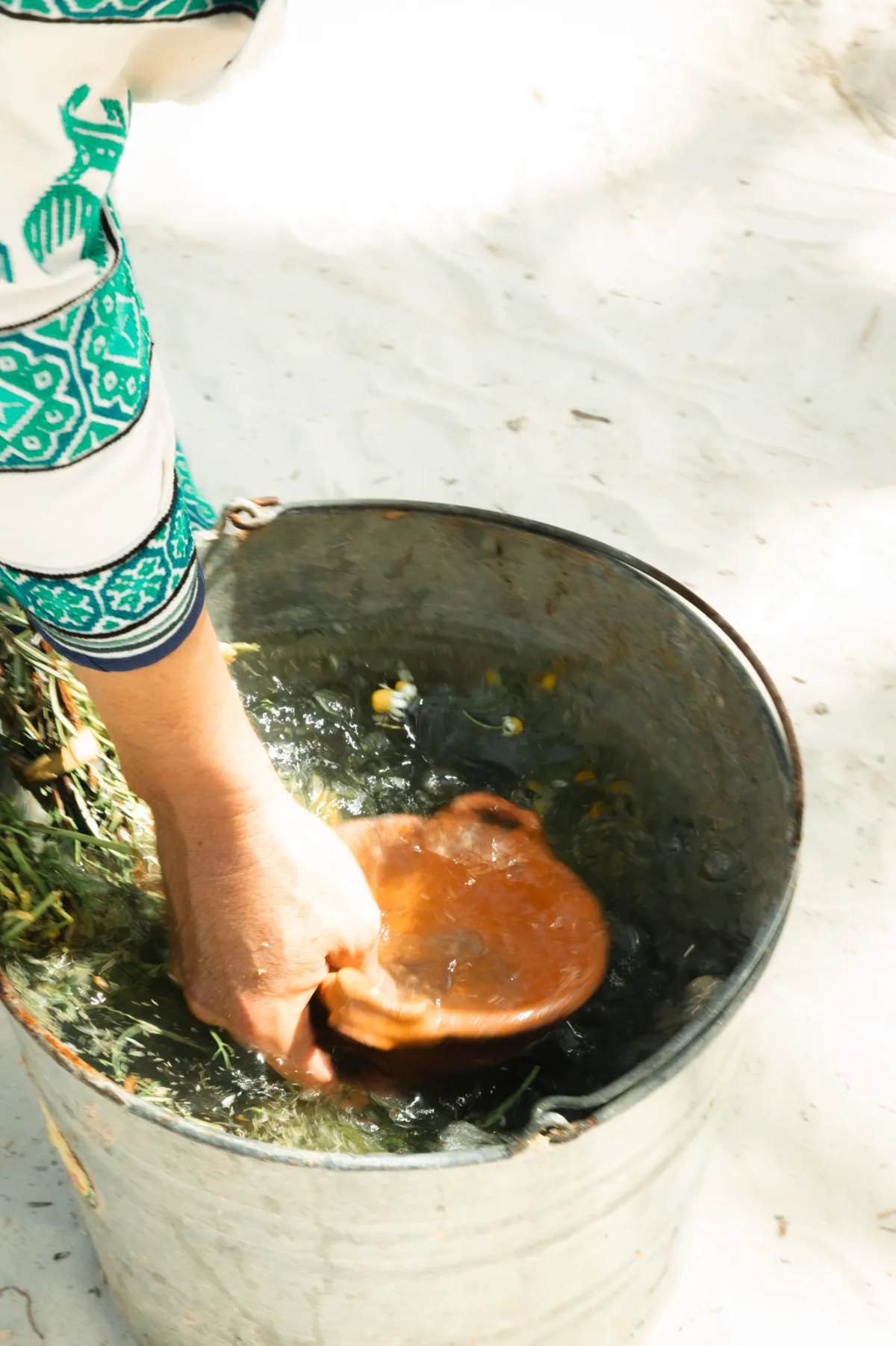 Mano sumergiendo un plato en agua dentro de un balde de metal.