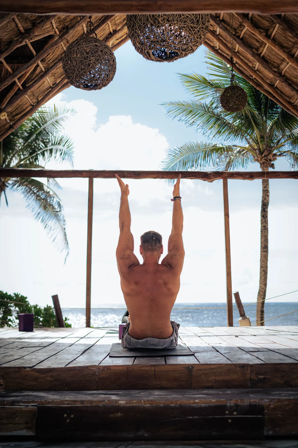 Persona haciendo yoga frente al mar bajo un techo de palapa.