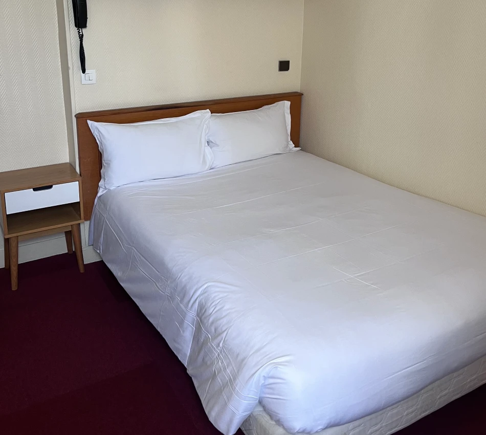 Lit double avec draps blancs et table de chevet en bois.