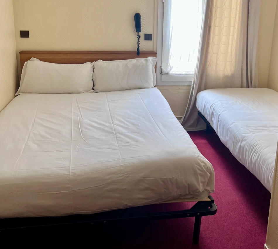 Deux lits avec draps blancs dans une chambre à la moquette rouge.