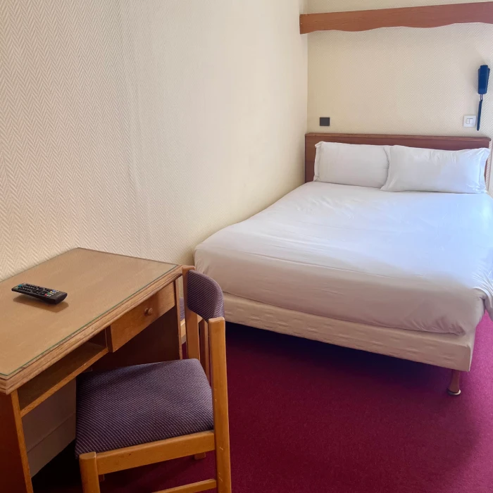 Chambre simple avec lit double, bureau, chaise, et télécommande.