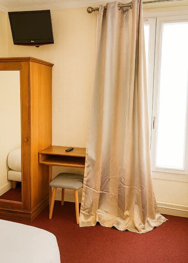 Petite chambre d'hôtel avec armoire, télé, rideaux et bureau.