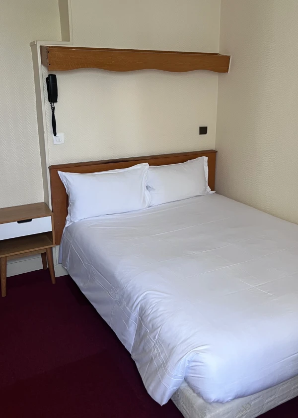 Lit double avec draps blancs dans une chambre d'hôtel simple.