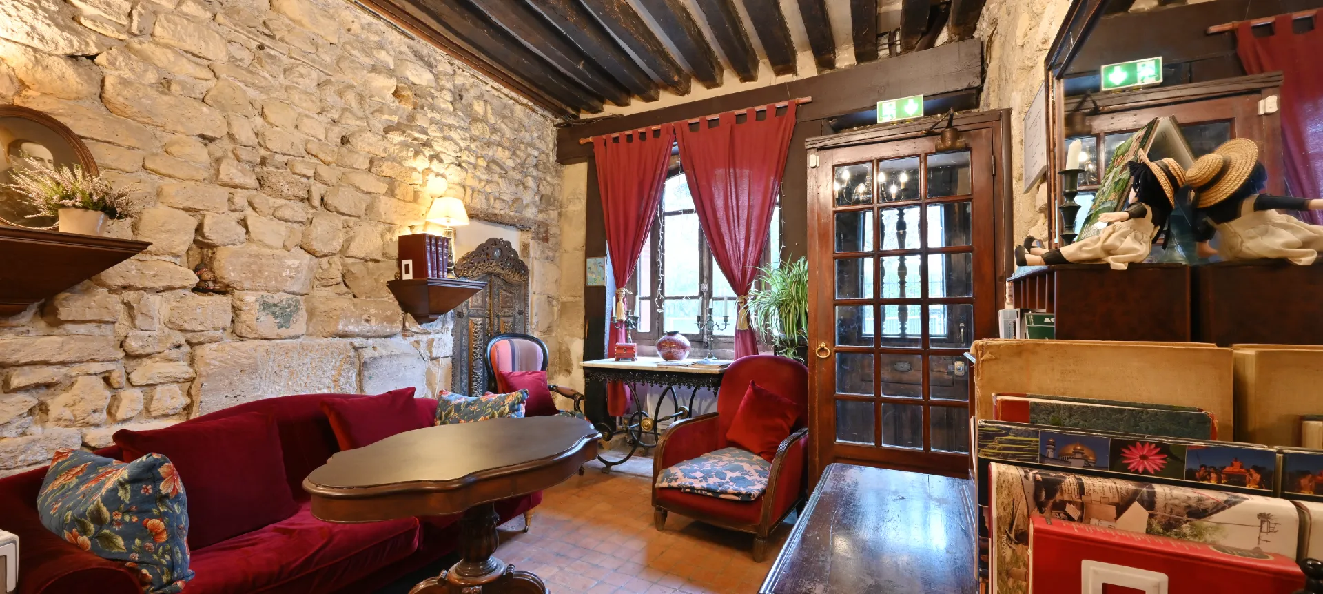 Sala rústica con paredes de piedra, sofás rojos, mesa de madera y cortinas granate.