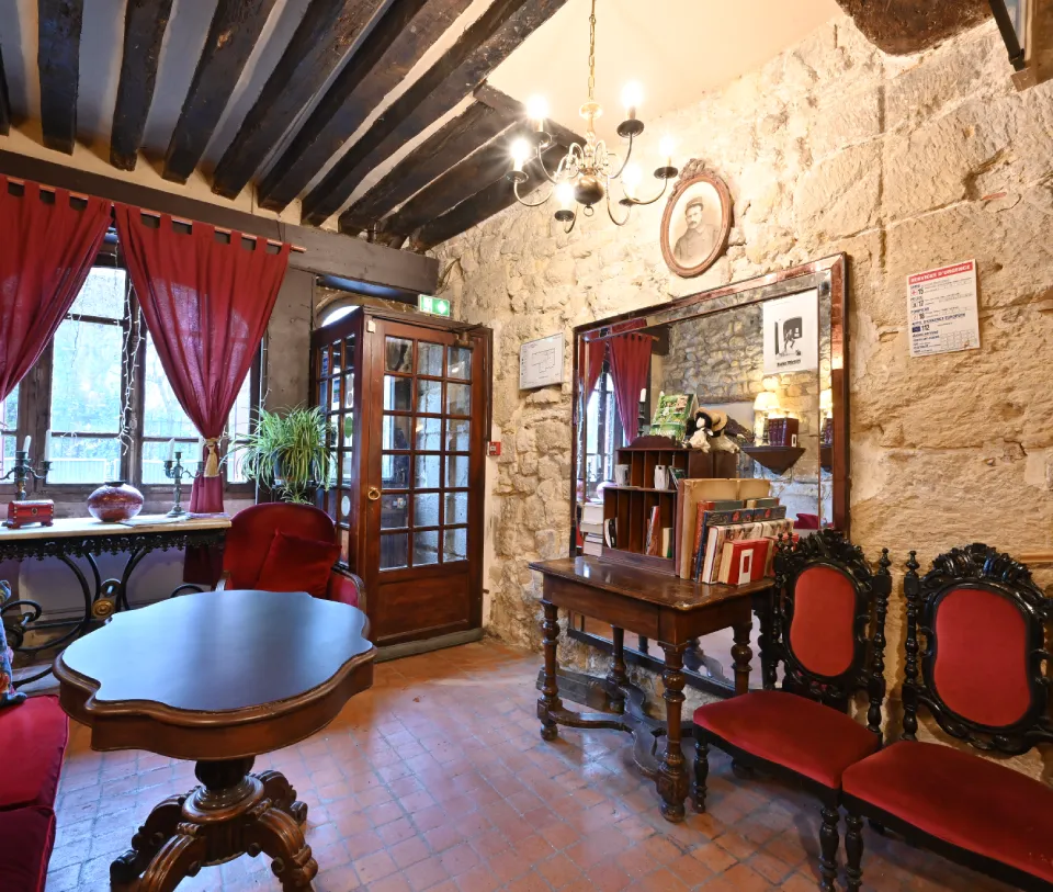 Sala con muebles antiguos, paredes de piedra, cortinas rojas y l&aacute;mpara de ara&ntilde;a.