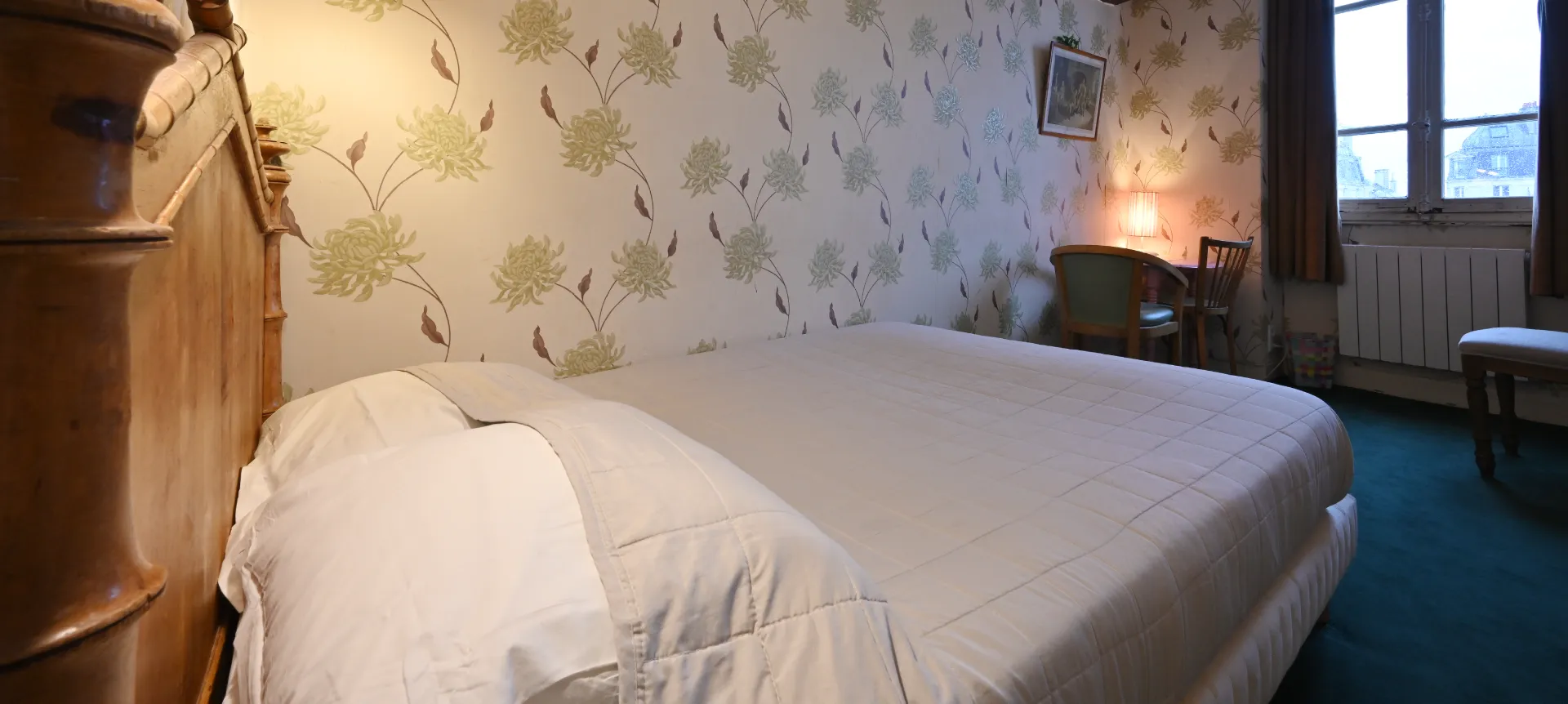 Habitación con cama grande, papel tapiz floral y ventana con cortinas marrones.