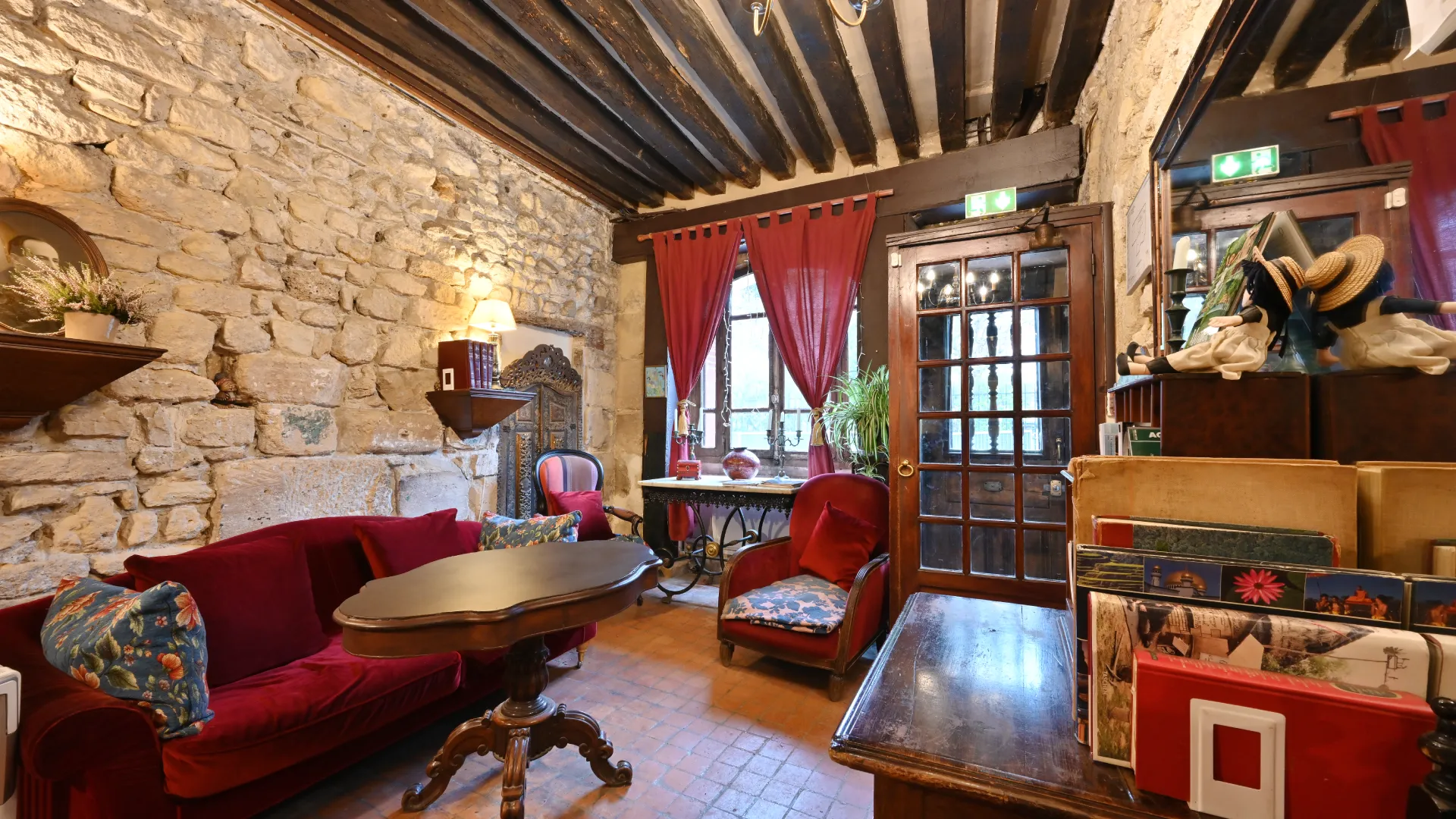 Sala vintage con paredes de piedra, cortinas rojas y muebles antiguos de madera y terciopelo.