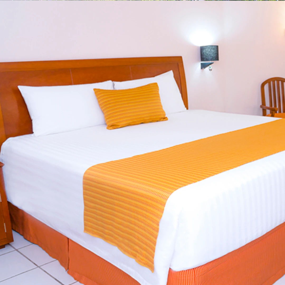 Cama con cabecera de madera, ropa blanca y cubrecama naranja. Luces de pared e interior simple y acogedor.