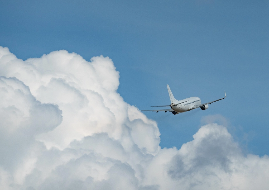 Avion volant haut dans un ciel bleu clair, entour&eacute; de nuages blancs cotonneux.